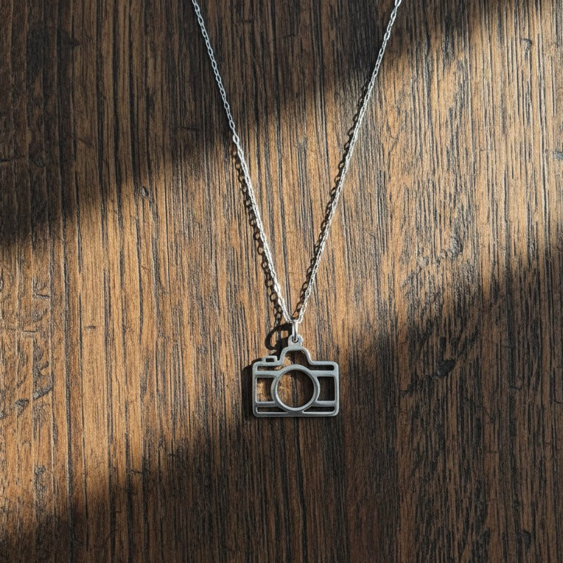 Camera-shaped pendant on a chain against a wooden background