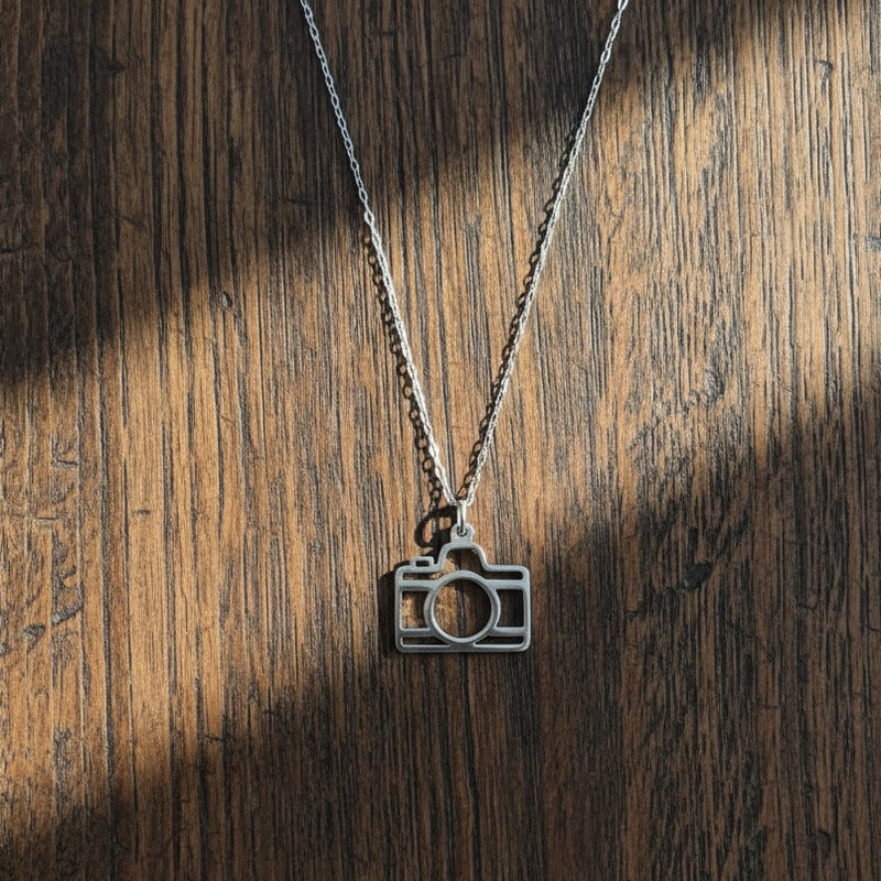 Camera-shaped pendant on a chain against a wooden background